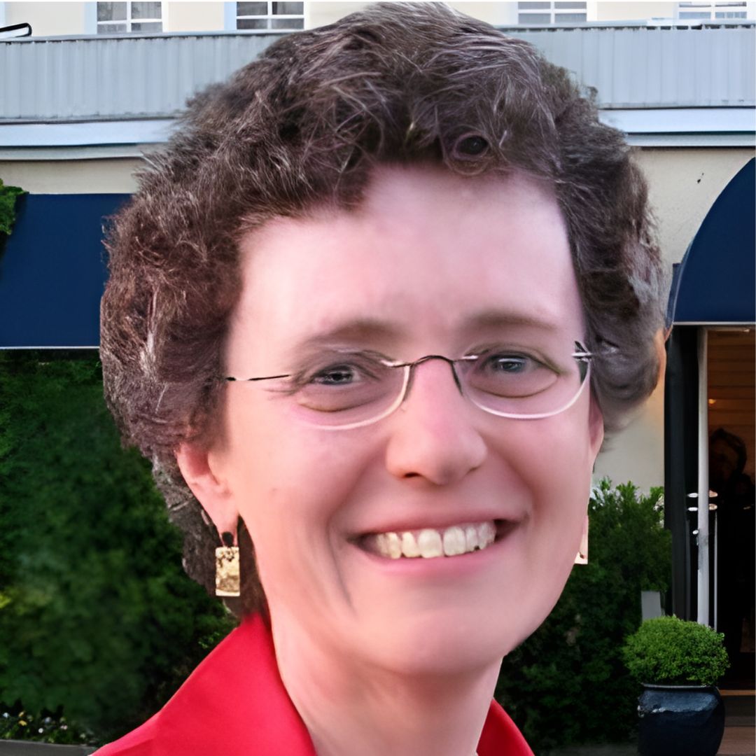 A photo of a woman wearing a red collared top, glasses, and smiling.