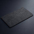 A dark gray felt desktop pad with rounded corners, shown at an angle on a dark gray textured background.