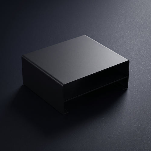 A matte black rectangular metal monitor riser with a low-profile base, shown on a dark textured background.