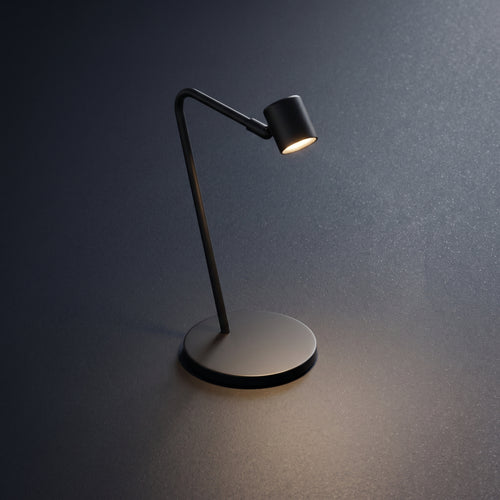 A modern black adjustable desk lamp with a circular base and curved arm, shown lit against a dark gray textured background.